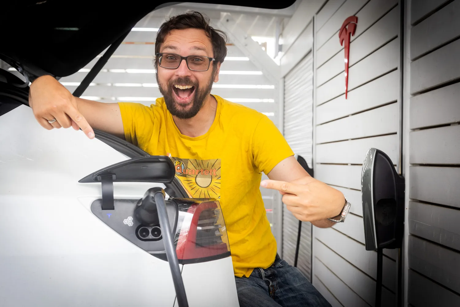 Jörg u otevřeného nabíjecího portu své Tesly před nabíječkou Tesla Wall Connector