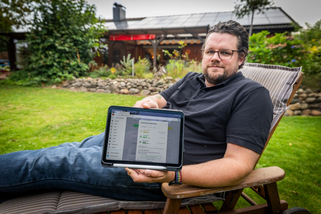 Bastian mit iPad vor Haus mit PV-Anlage