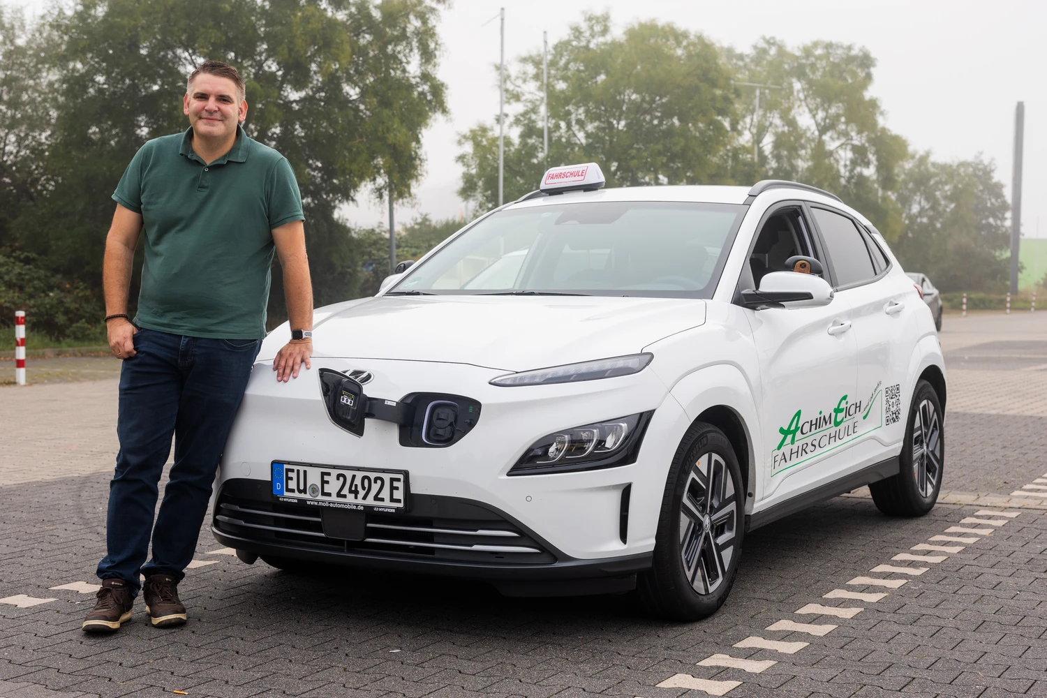 Alex in front of driving school car with open charging port